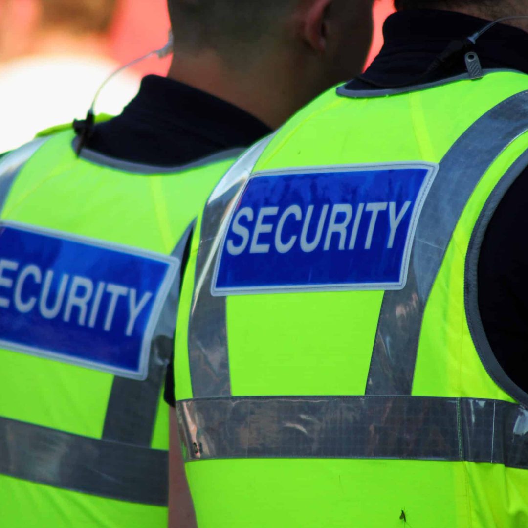 Image of two male security Guards with bright tops on.